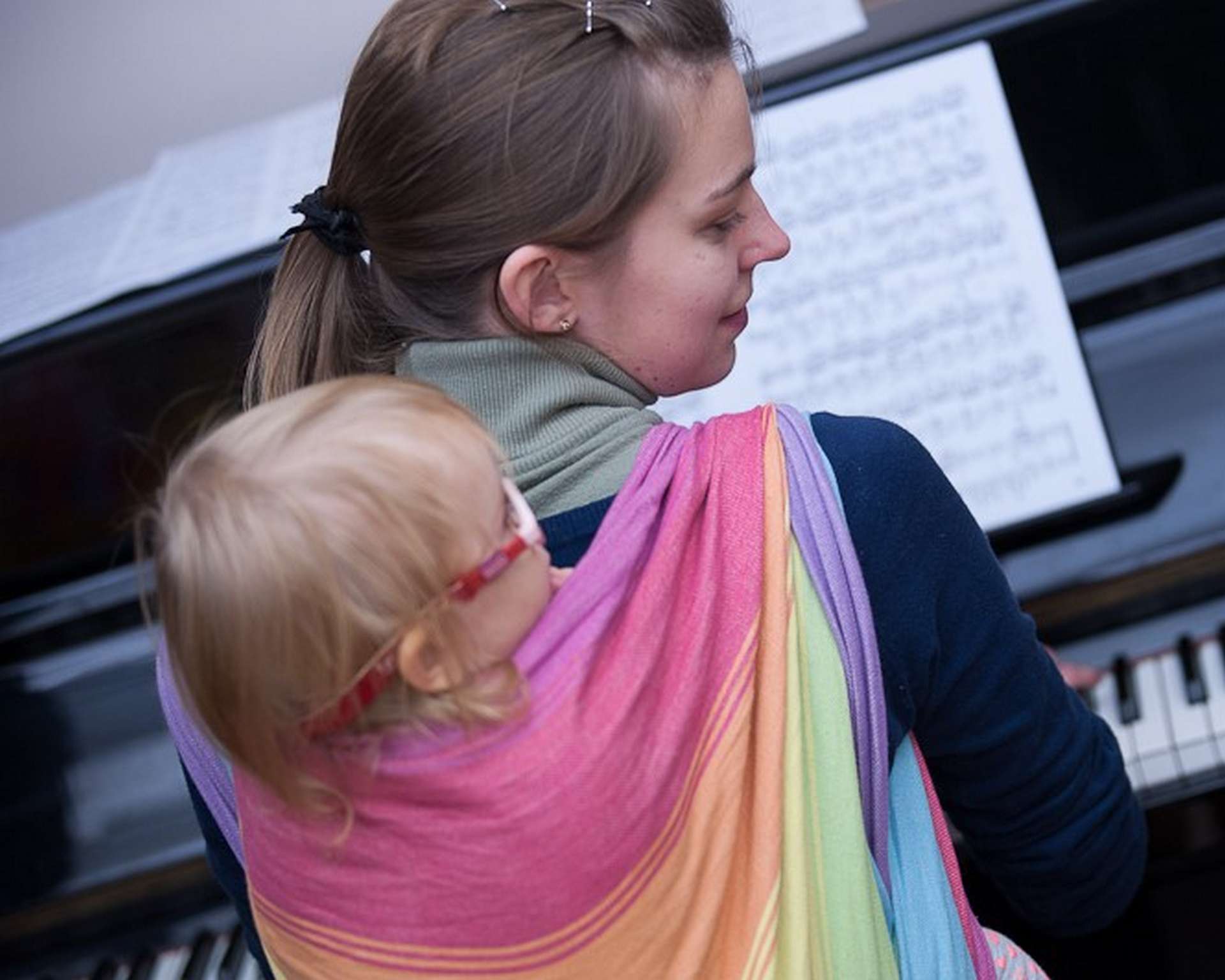 Elwira Kowal-Budziak z dzieckiem w chuście na plecach gra na pianinie.